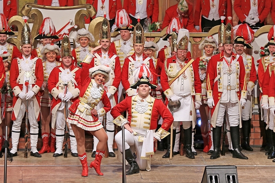Foto der Ehrengardisten auf der Bühne der großen Bürgersitzung, im Hintergrund stehen die Gardisten und im Vordergrund post das Tanzpaar