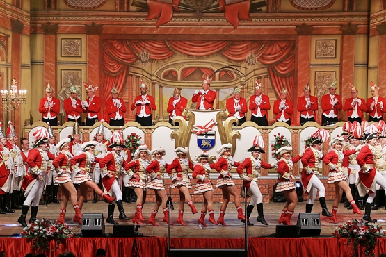 Foto der Bühne der großen Bürgeritzung, im Hintergrund steht der Elferrat auf dem Podest und klatscht während im Vordergrund die Tanzgrupppe alles gibt