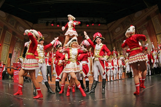 Ein Foto der Tanzgruppe in Aktion auf der Bühne, tanzende Gardisten im Vordergrund und im Hintergrund stehen Gardisten und feiern