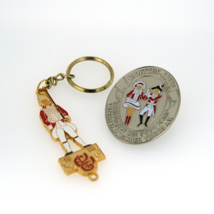 Foto von einem Pin und einem Schlüsselanhänger Ein goldener Schlüsselanhänger der Ehrengarde und ein Silberner Pin des Cadettencorps