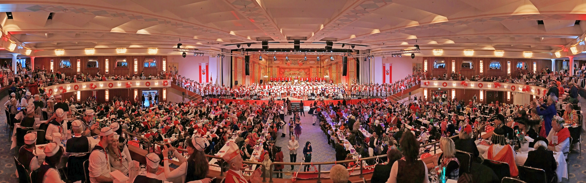 Der große Saal ist gefüllt mit zahlreichen Gästen, auf der Bühne sind die Ehrengardisten und Ehrengardistinnen in ihren traditionellen Roten Uniformen zu sehen.