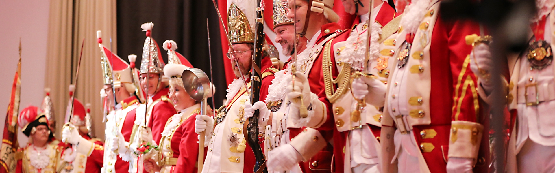 Vertreter aller Formationen stehen auf der Bühne, sie halten Waffen wie Degen, Bajonett oder Suppenkelle in den Händen.