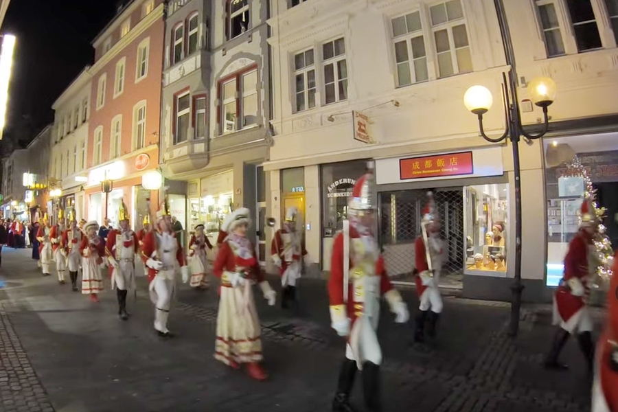 Screenshot aus dem Video der EhrenGarde des Wachhäuschenaufstellfestes der Kavallerie 2020: Die Ehrengardisten ziehen marschierend durch die nächtliche Friedrichstraße. Durch das Klicken wird das Video abgespielt.